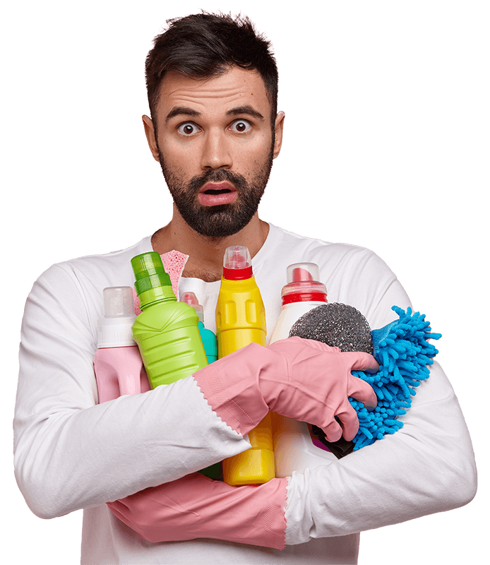 A surprised man in a white shirt holds various cleaning supplies, including bottles and a sponge, while wearing pink rubber gloves. The background is black, emphasizing his expression and the cleaning products.